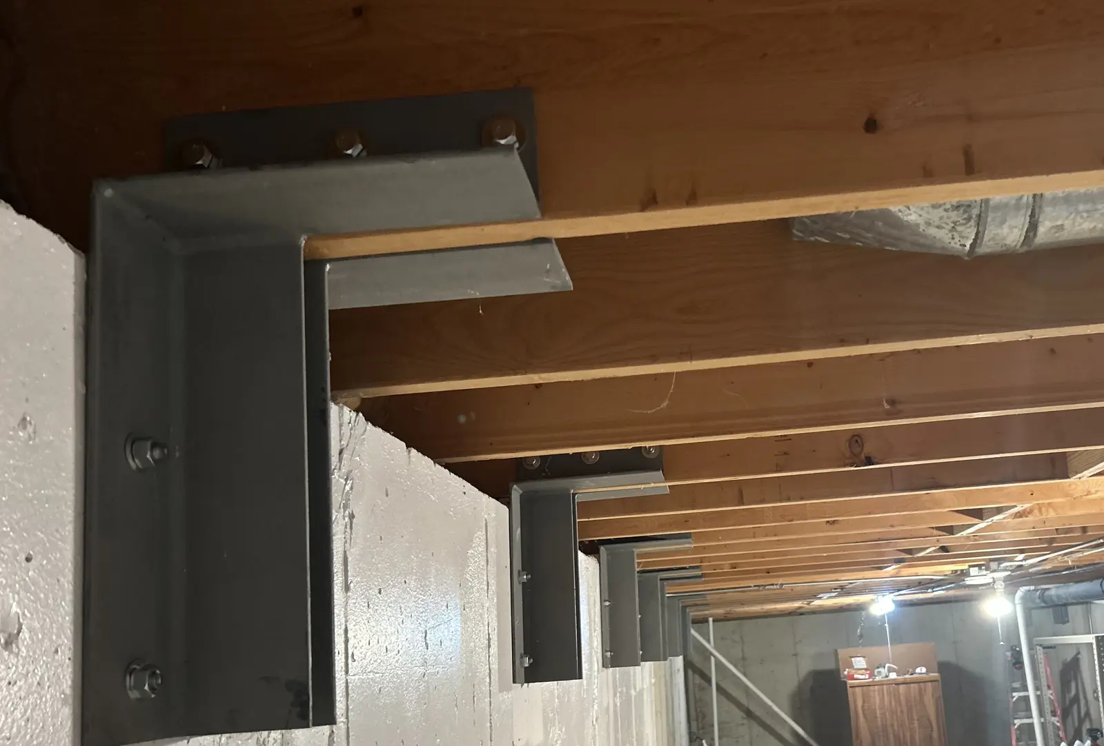 22 custom steel brackets reinforcing a bowing basement foundation wall, tied into the floor joists above, Chicago suburbs
